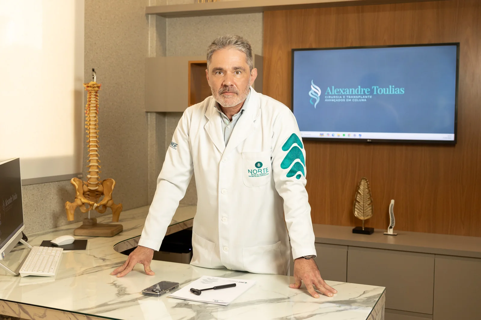 Dr. Alexandre Toulias no consultório com modelo anatômico de coluna